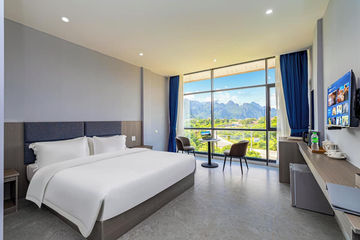 A modern hotel room with a large bed, a desk, and a view of mountains through the window.