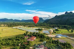 A hot air balloon flying over a rural landscape with fields, houses, and mountains.