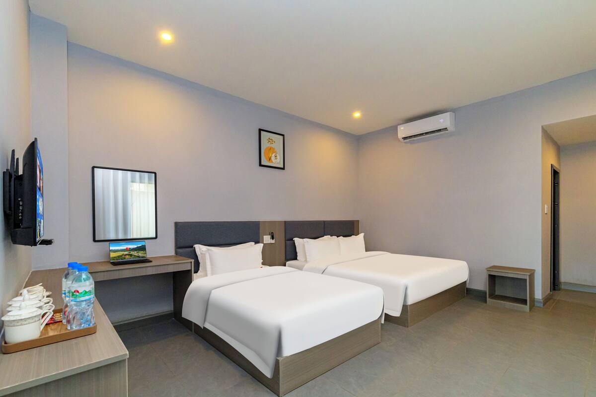 A hotel room with two beds, a desk with a laptop, a TV, and a water bottle.