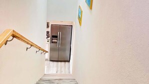 Un escalier étroit avec une rampe en bois mène à un espace cuisine équipé d’un réfrigérateur en acier inoxydable.