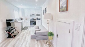 Une cuisine moderne avec des meubles blancs, un coin repas avec un canapé et un couloir agrémenté d’une lampe et d’une porte.
