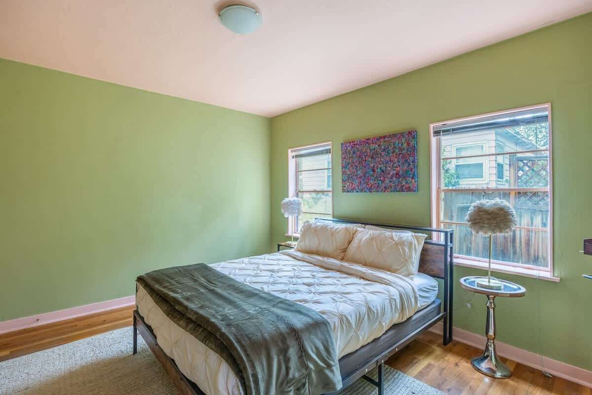 A bedroom with a bed, a round table, a window, and a wall art piece.