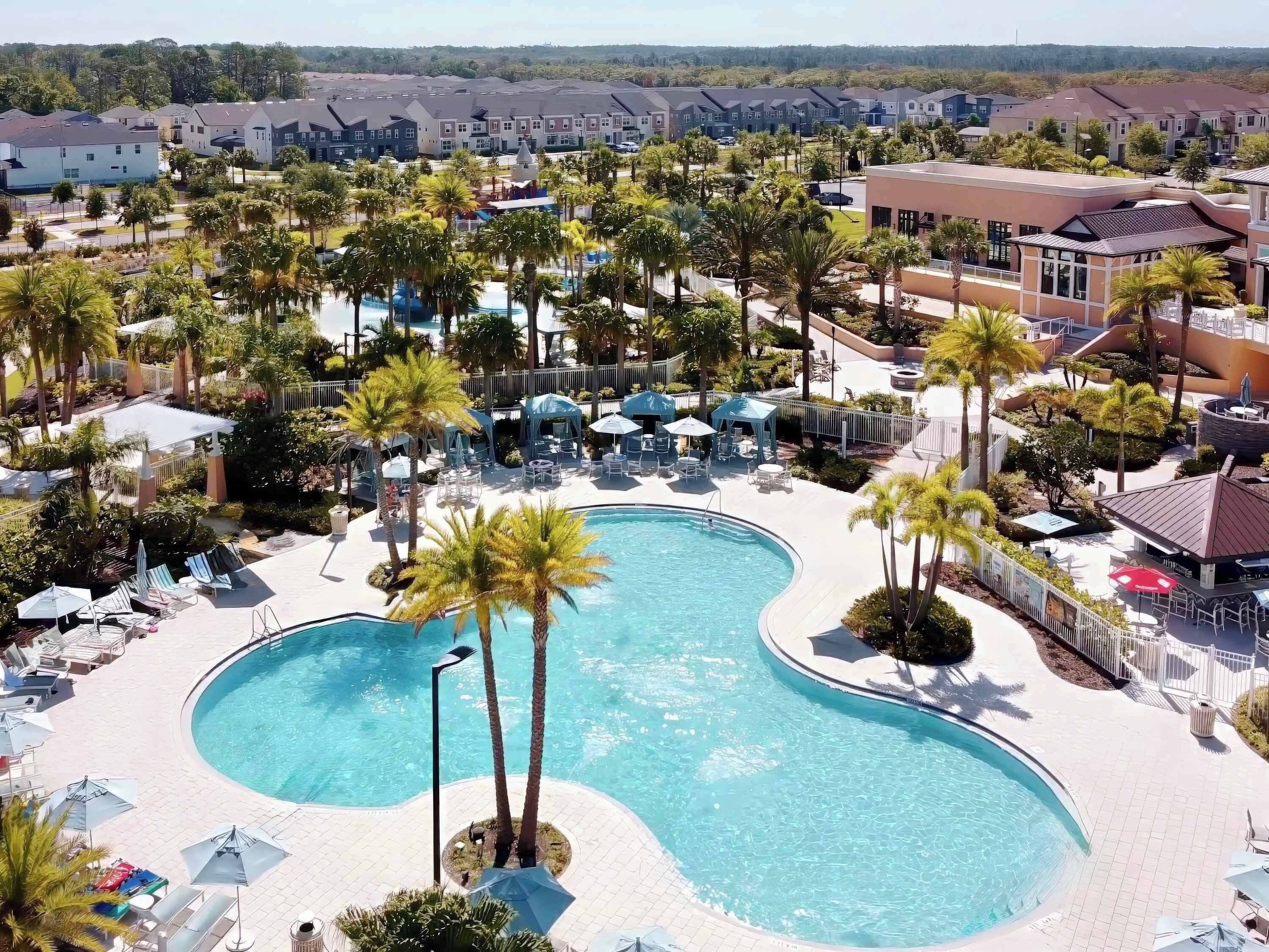 Un complexe hôtelier doté d’une grande piscine incurvée, entourée de palmiers et de chaises longues.