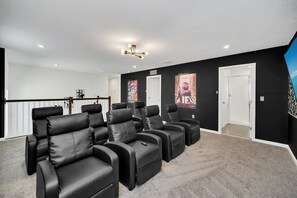 Une salle de cinéma privée avec des fauteuils en cuir noir inclinables, un sol recouvert de moquette et un plafond blanc doté d’un éclairage encastré.