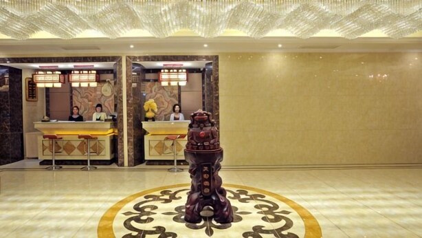 Un área de recepción con mostrador, dos recepcionistas y una estatua decorativa en el centro.