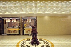 A reception area with a reception desk, two receptionists, and a decorative statue in the center. - Shangwei Hotel (Dongyang)