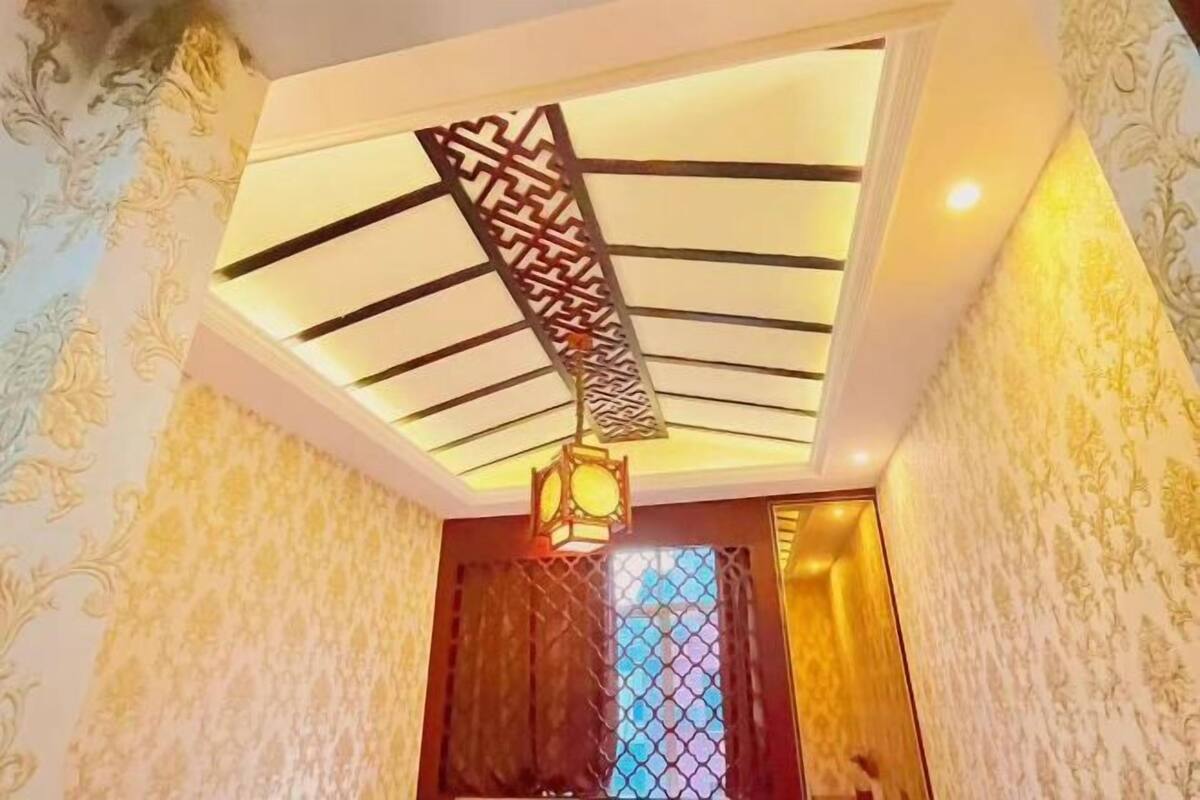 A room with patterned wallpaper, a decorative ceiling light fixture, and a wooden door with a window.