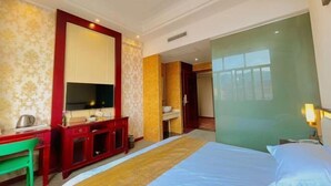 Habitación de hotel con cama, escritorio, televisor y baño visible a través de una puerta abierta.