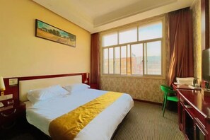 A hotel room with a bed, a desk, a chair, a television, and a window with curtains. - Shangwei Hotel (Dongyang)