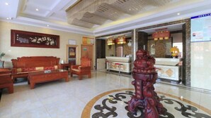 Un hall con mostrador de recepción, un conjunto de sofás de madera y una estatua decorativa.