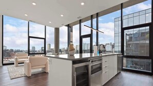 Een moderne keuken met een groot eiland, roestvrijstalen apparatuur en een stadsgezicht door grote ramen.