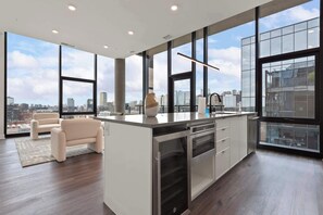 Una cocina moderna con una isla grande, electrodomésticos de acero inoxidable y vistas a la ciudad a través de amplios ventanales.
