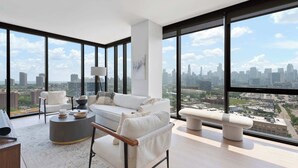Una sala de estar moderna con vista a la ciudad, que incluye un sofá, sillones, una mesa de centro y un banco.