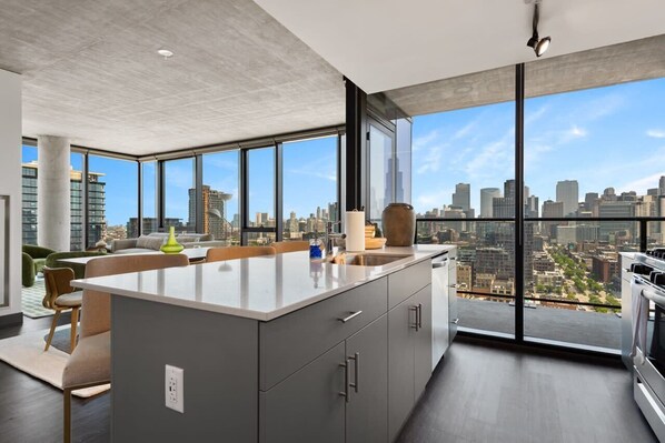 A modern kitchen with a large island, city views through large windows, and a minimalist design.