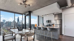 Cocina moderna con vista a la ciudad, un comedor con mesa y sillas, y una barra con taburetes.