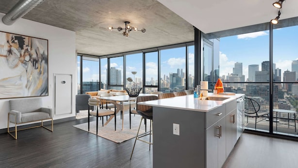 Una cocina moderna con una isla grande, comedor con sillas y vistas a la ciudad a través de amplios ventanales.