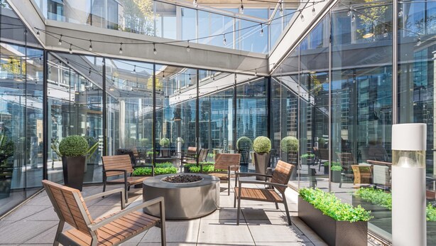 Un espace extérieur moderne, aménagé avec des murs en verre, des meubles en bois et des plantes en pot.