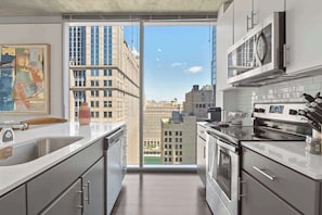A modern kitchen with a large window, stainless steel appliances, and a view of city buildings.