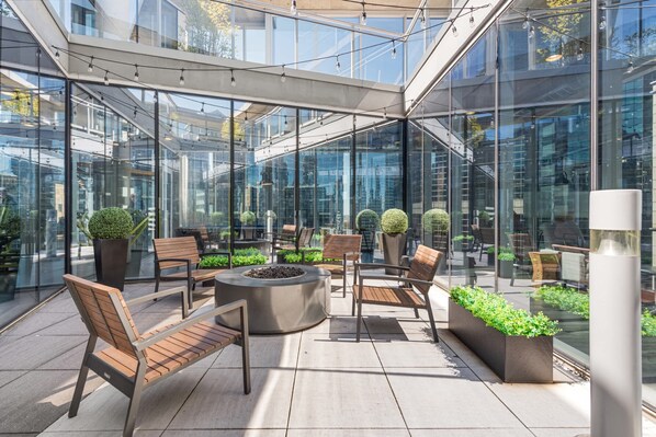A modern outdoor seating area with glass walls, wooden furniture, and potted plants.