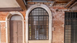 Fachada d'un edifici amb una gran finestra d'arc rodó amb baranes metàl·liques, una porta de fusta i un mur de rajola.