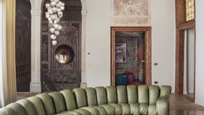 Un sofà verd de cuir corbat en una habitació amb terra de marbre, una taula de centre rodona i un penjoll decoratiu a la paret.