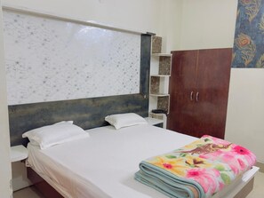 A bedroom with a bed, white pillows, a wooden headboard, a wardrobe, and a patterned wall. - Hotel Ashoka By GRB (Sheikhpura)