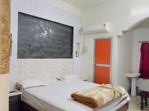 Ein Schlafzimmer mit einem Bett, einem Nachttisch, einer Wand-Klimaanlage, einer orangefarbenen Tür und einem Badezimmer mit Waschbecken und einem roten Vorhang.