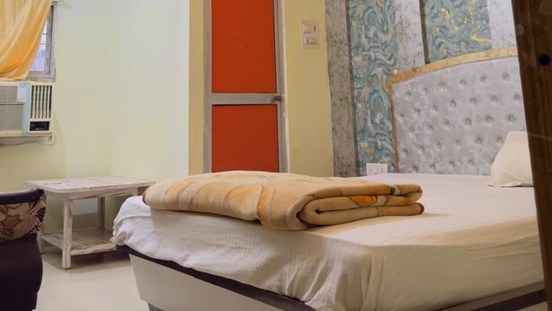 Une chambre à coucher comprenant un lit, un ventilateur de plafond, une fenêtre avec des rideaux, un radiateur et un mur orné d’un panneau décoratif.