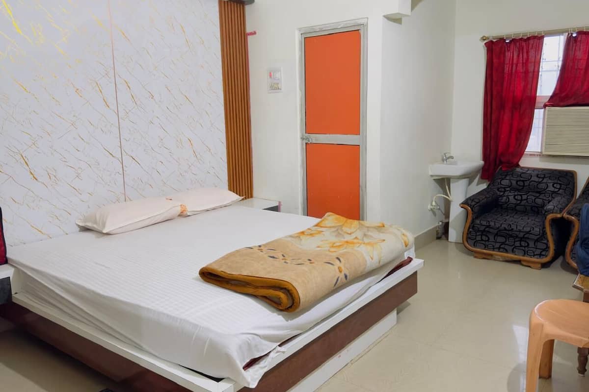 Quarto de hotel com cama, uma cadeira, pia e janela com cortinas vermelhas.