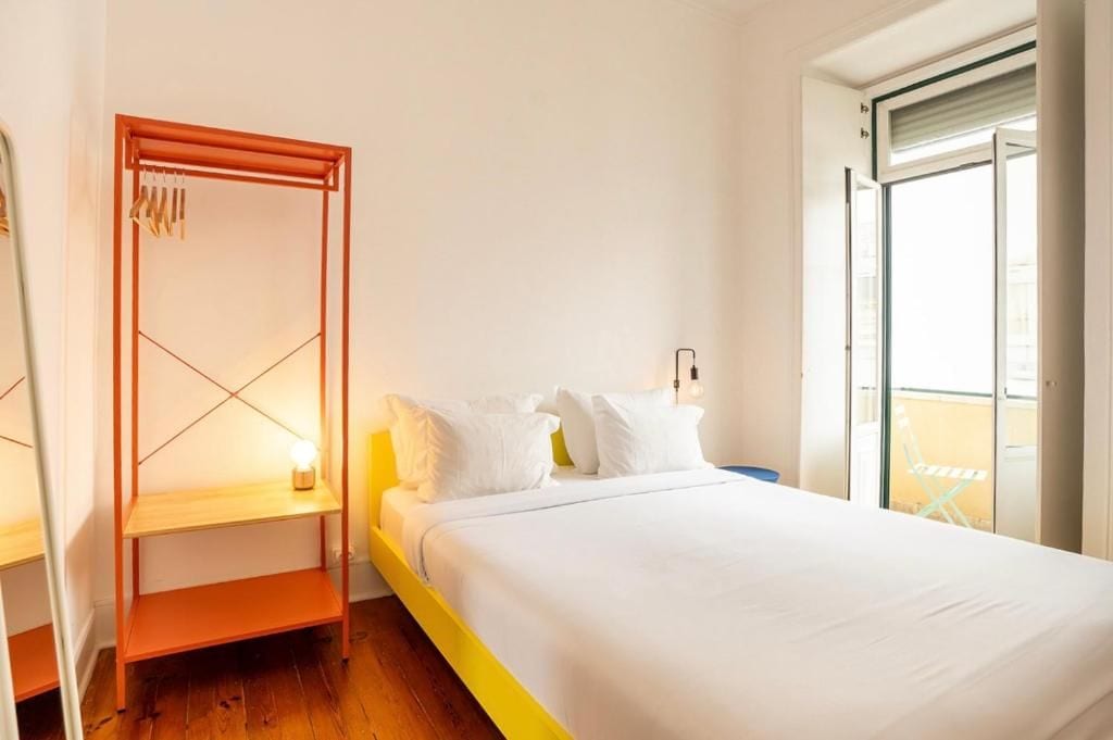 A bedroom with a bed, a wooden shelf unit, and a window with a view.