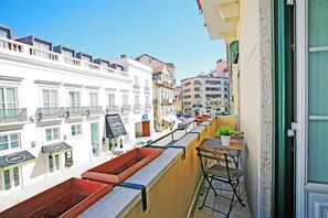 A balcony with a view of a street lined with buildings, a small table with a plant, and a red planter. - SATURdAYS (Lisbon)