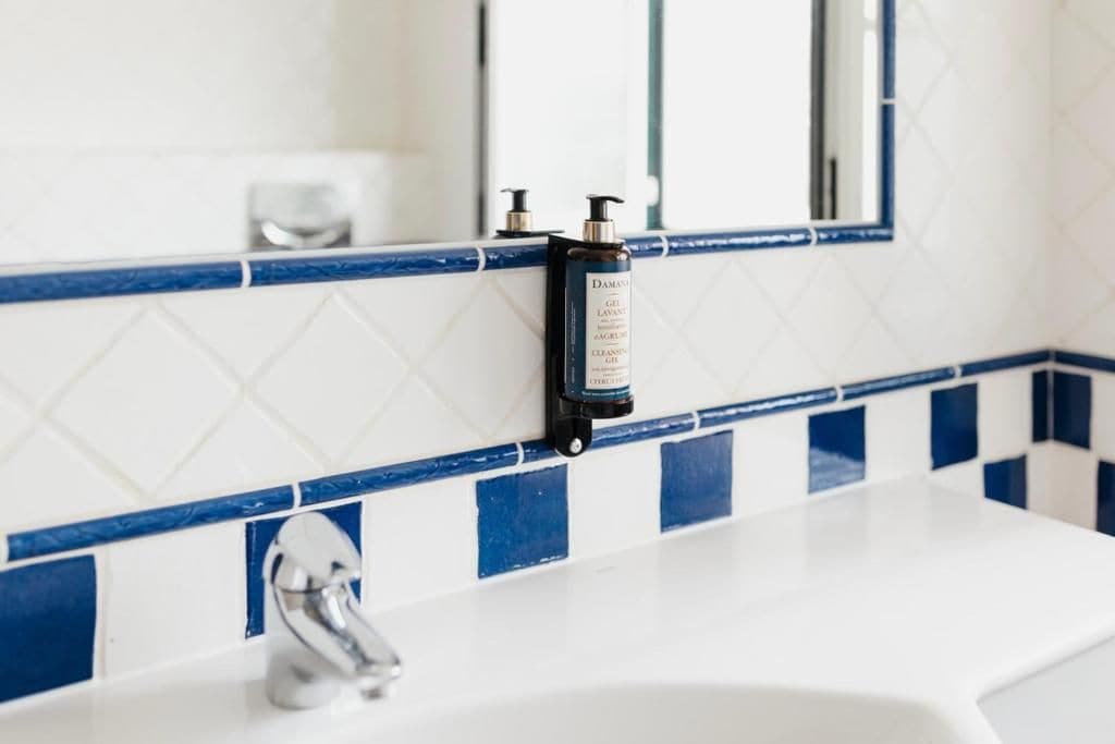 A bathroom with a white sink, a mirror, and a bottle of shampoo.