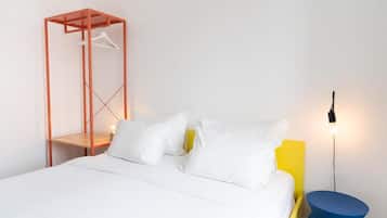 A bed with white bedding, a hanging garment organizer, a bedside table with a lamp, and a yellow accent wall.