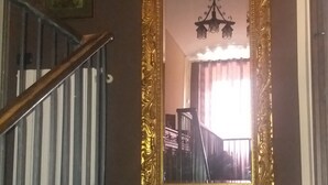 Eine Treppe mit schwarzer Handläufe führt zu einer Zwischenebene. Ein großer, aufwendig gestalteter Spiegel mit goldener Rahmung ist an der Wand oberhalb der Treppe angebracht.