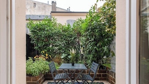 A patio with a table and chairs, surrounded by plants and a brick wall. - Geranimus Versailles Charost (Versailles)