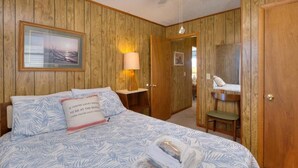 Una camera da letto con pannelli in legno, un letto con lenzuola fantasia, una lampada da comodino, una ventola a soffitto e un quadro appeso al muro.