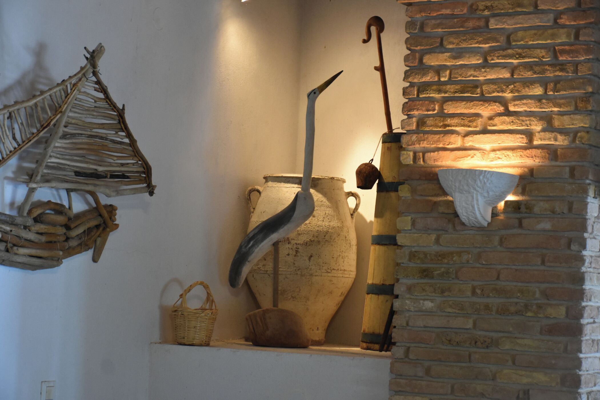 A rustic interior with a large ceramic pot, a wooden basket, and a wall-mounted light fixture.