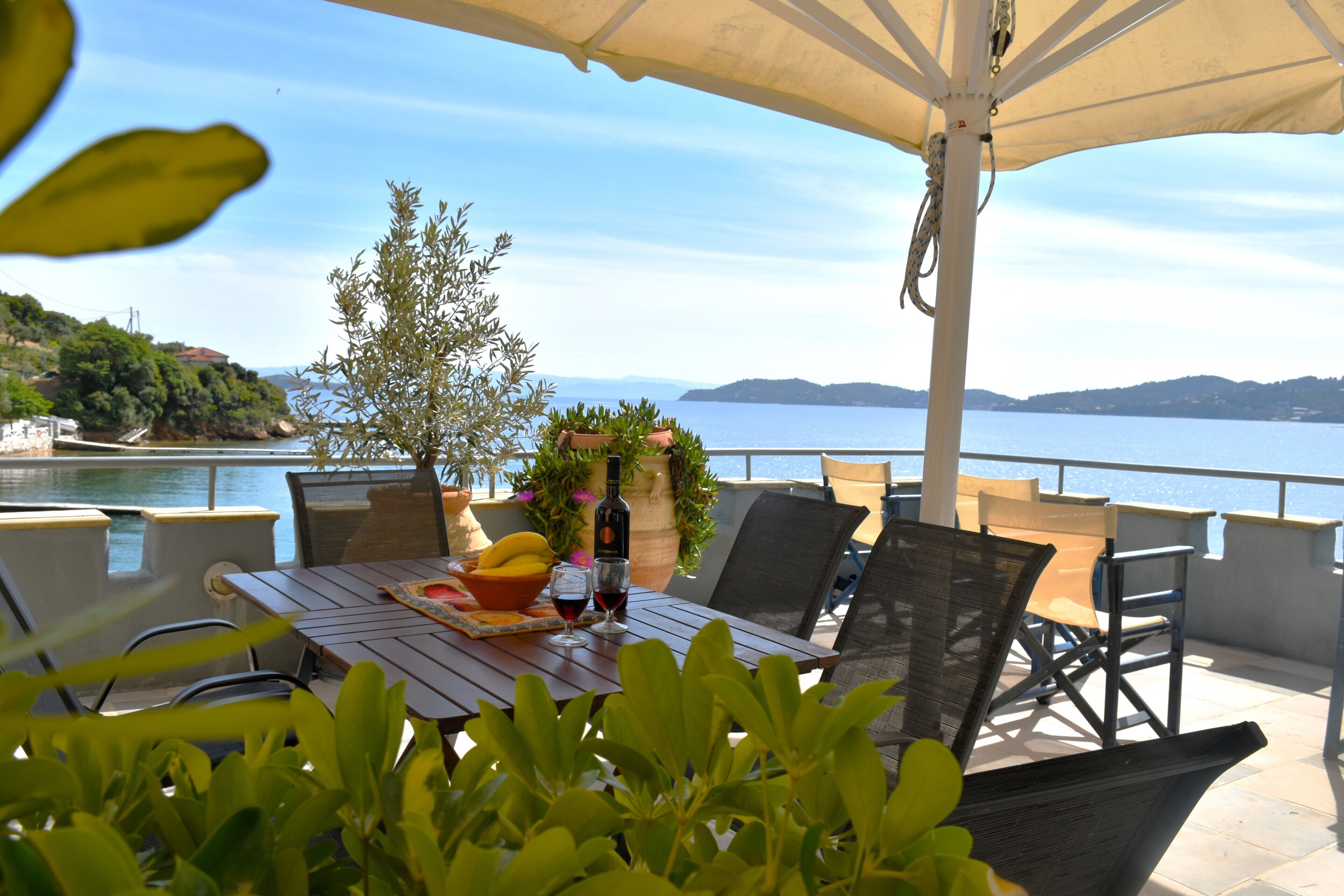 A terrace with a table set for dining, overlooking a body of water and hills.