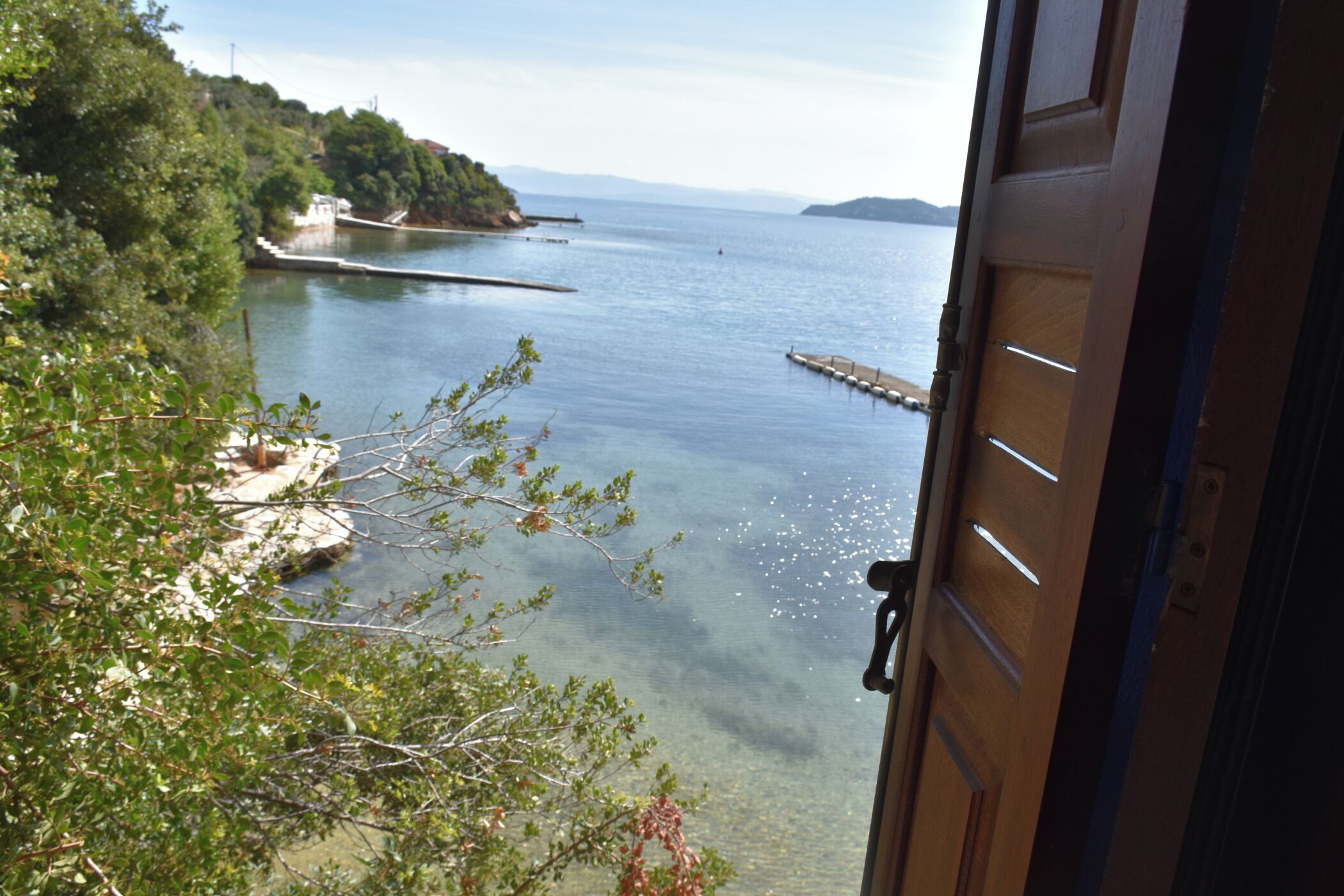 A view through an open door of a coastal area with clear water, a dock, and greenery.