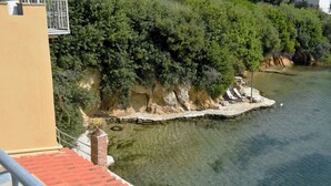 Blick auf die Küste mit klarem Gewässer, felsiger Uferlinie und einem Gebäude mit roten Ziegeln.