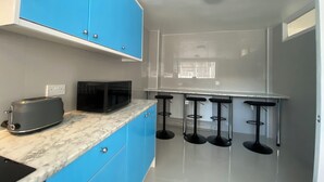 Una cocina moderna con armarios azules, encimera de mármol, un tostador, un microondas y tres taburetes de bar.
