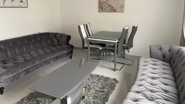 Una sala de estar moderna con un sofá gris, una mesa de centro y una mesa de comedor con sillas.