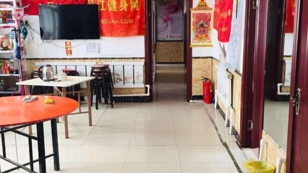 A hallway with a table and chairs, a television mounted on the wall, and a red banner with Chinese characters. - Xuegushanliren (Wuchang)
