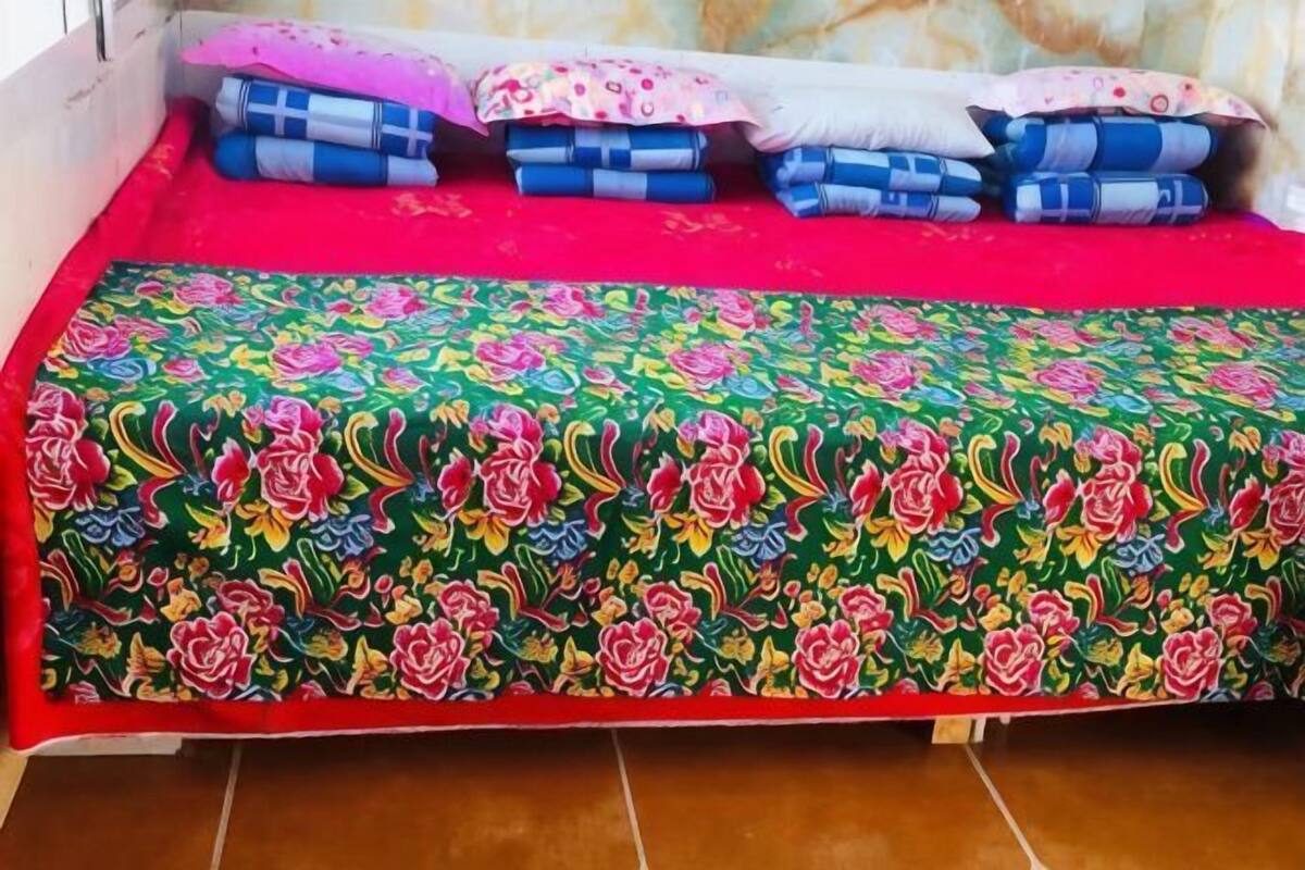 A bed with a colorful floral bedspread, pillows, and a red blanket.