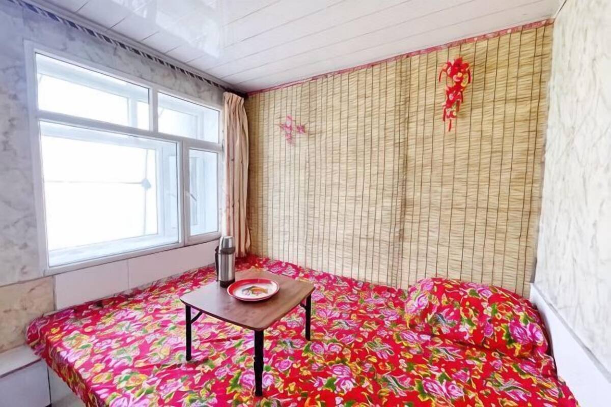 A room with a bed, a window, a table with a plate, and a curtain.