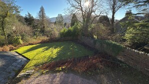 Un patio trasero con césped, un muro de piedra, árboles y una montaña al fondo.