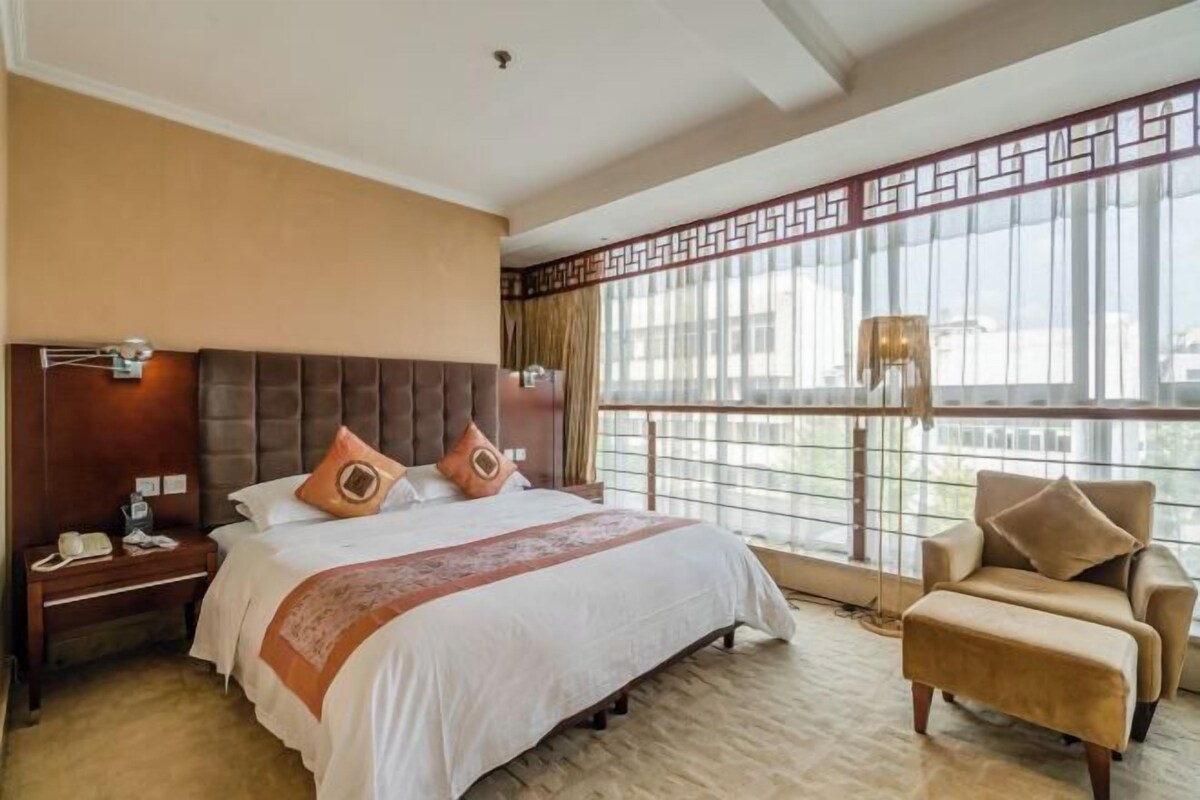 Habitación de hotel con una cama grande, una mesita de noche, una silla y un amplio ventanal con vistas.