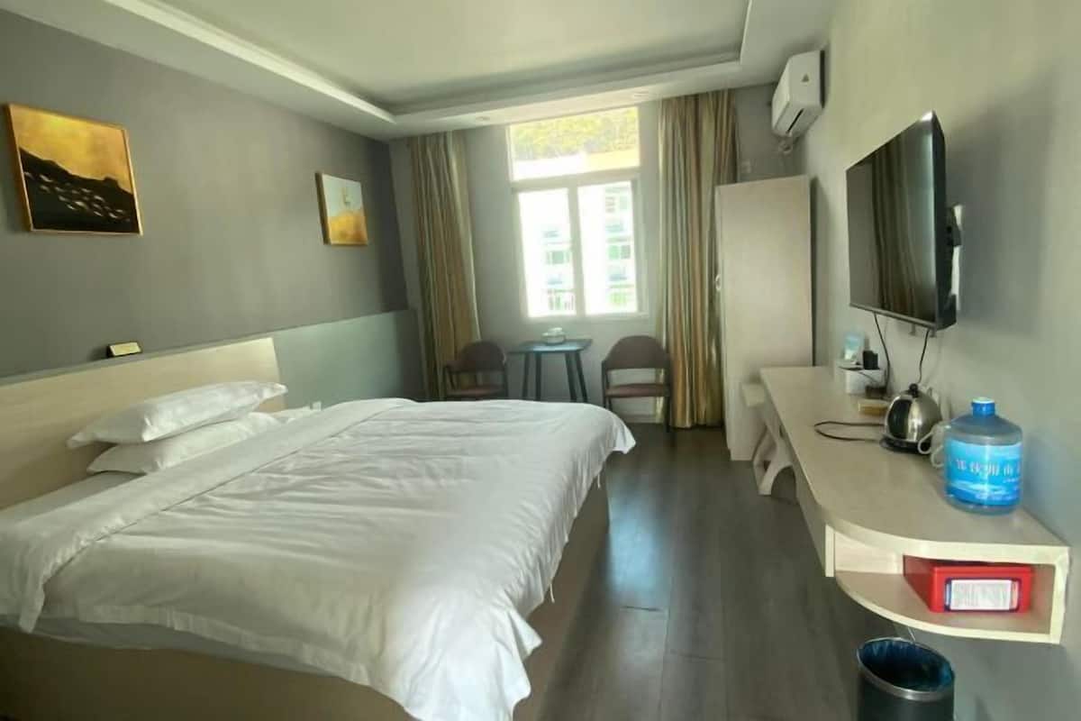 A hotel room with a bed, a desk, a chair, a TV, and a window with curtains.