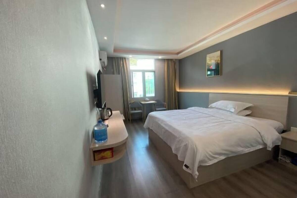 A hotel room with a bed, bedside table, TV, and a window with curtains.