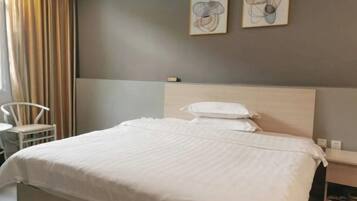 A neatly made bed with white bedding, a white chair, and two abstract paintings on the wall.